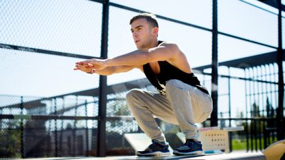 white man squatting with arms outstretched in a park 