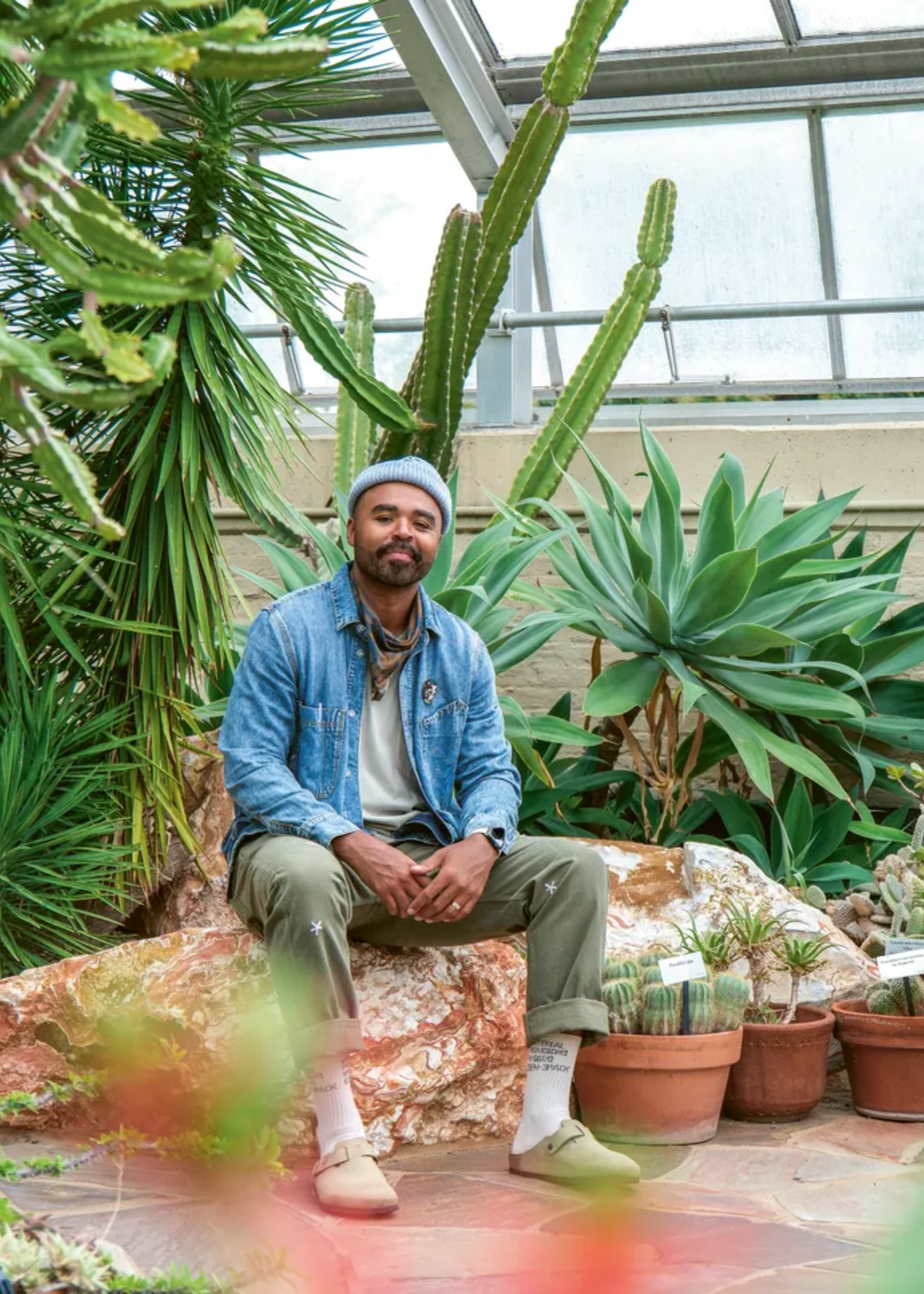 Hilton Carter sitting on a rock alongside his houseplant collection