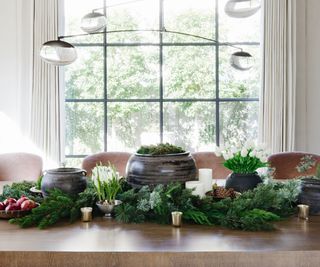 Christmas table with evergreen foliage, seasonal fruit, votive candles and ceramic pots filled with moss