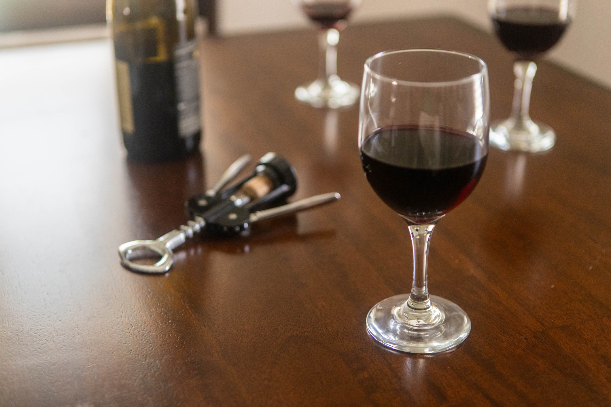 Red wine is shared on a table with other glasses.