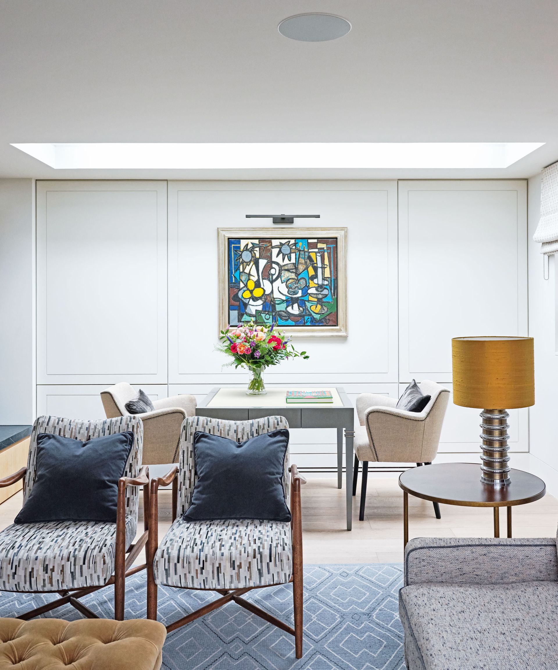 Two brown and cream chairs with dark blue cushions on next to a side table with an orange lamp in front of a dining table