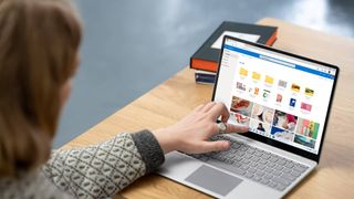 Student using Surface Laptop on a wooden desk next to text book