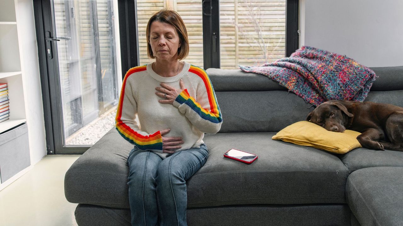 Woman sits on a sofa doing breathing exercises 