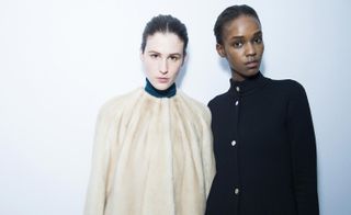 Two female models, one in a cream fur coat and one in a black coat