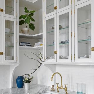 Corner of white kitchen with glass fronted cabinets