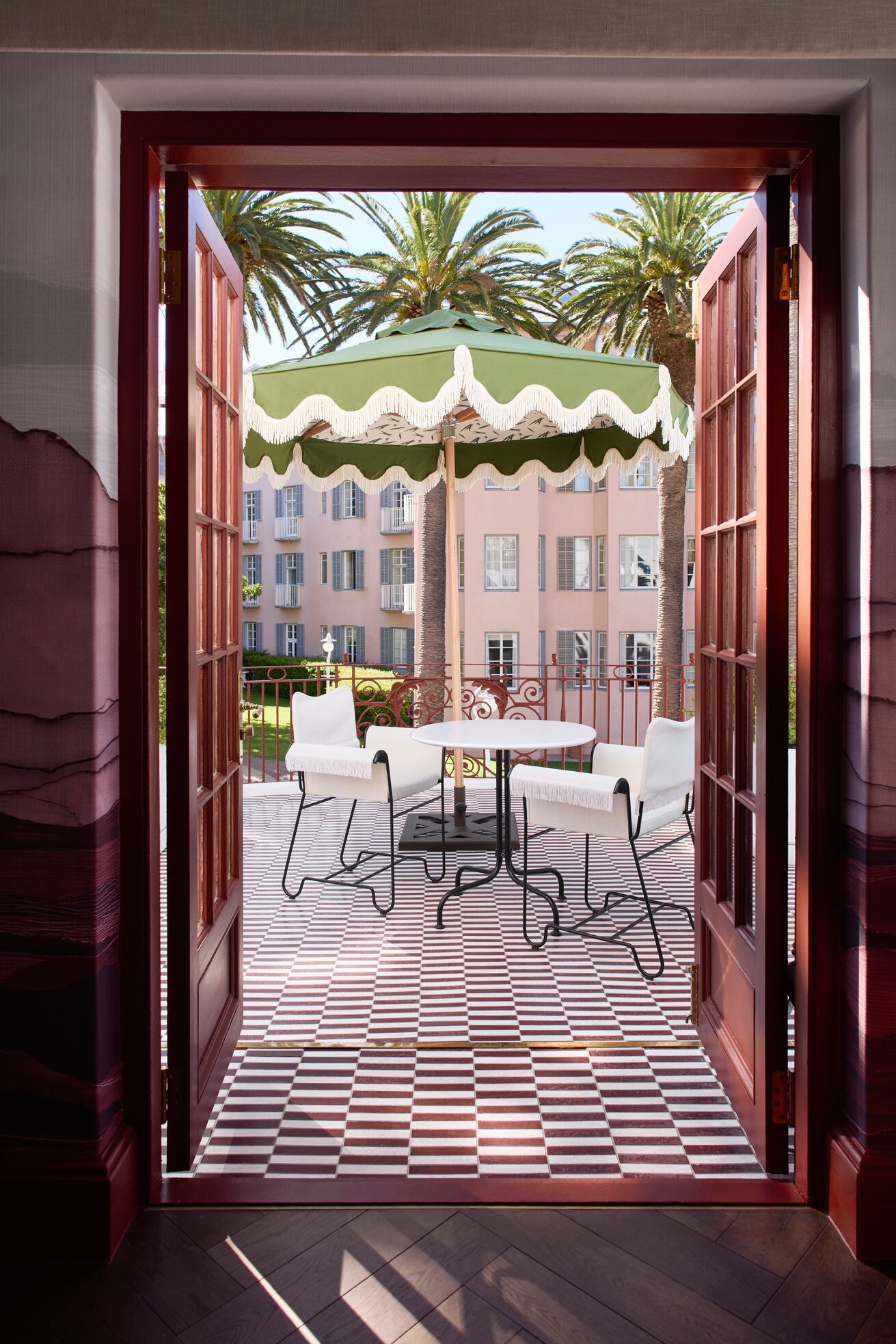 A series of shots capturing a young man dressed in patterned, or color-blocky, clothing, either standing in the sun-lit outdoor areas of a lush hotel, or inside a colorfully decorated suite filled with collectibles, artworks, and textural touches, or the interiors of that very space.