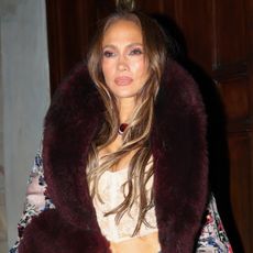 Jennifer Lopez wearing a long, opulent burnout velvet coat with a crop top and distressed jeans in Milan during MFW S/S 27