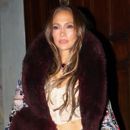Jennifer Lopez wearing a long, opulent burnout velvet coat with a crop top and distressed jeans in Milan during MFW S/S 27