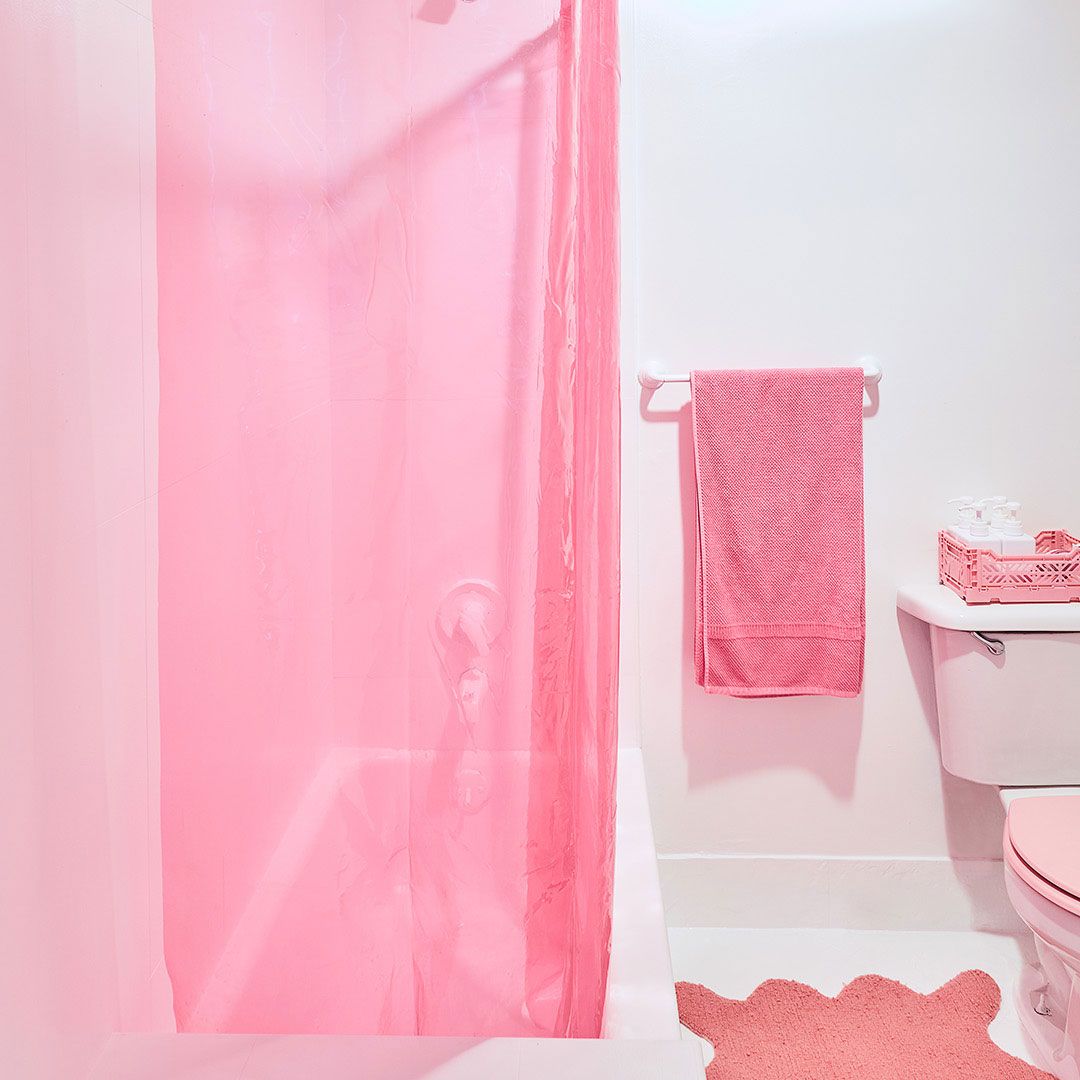 Kamar mandi dengan handuk merah muda, tirai shower, dan keset kamar mandi