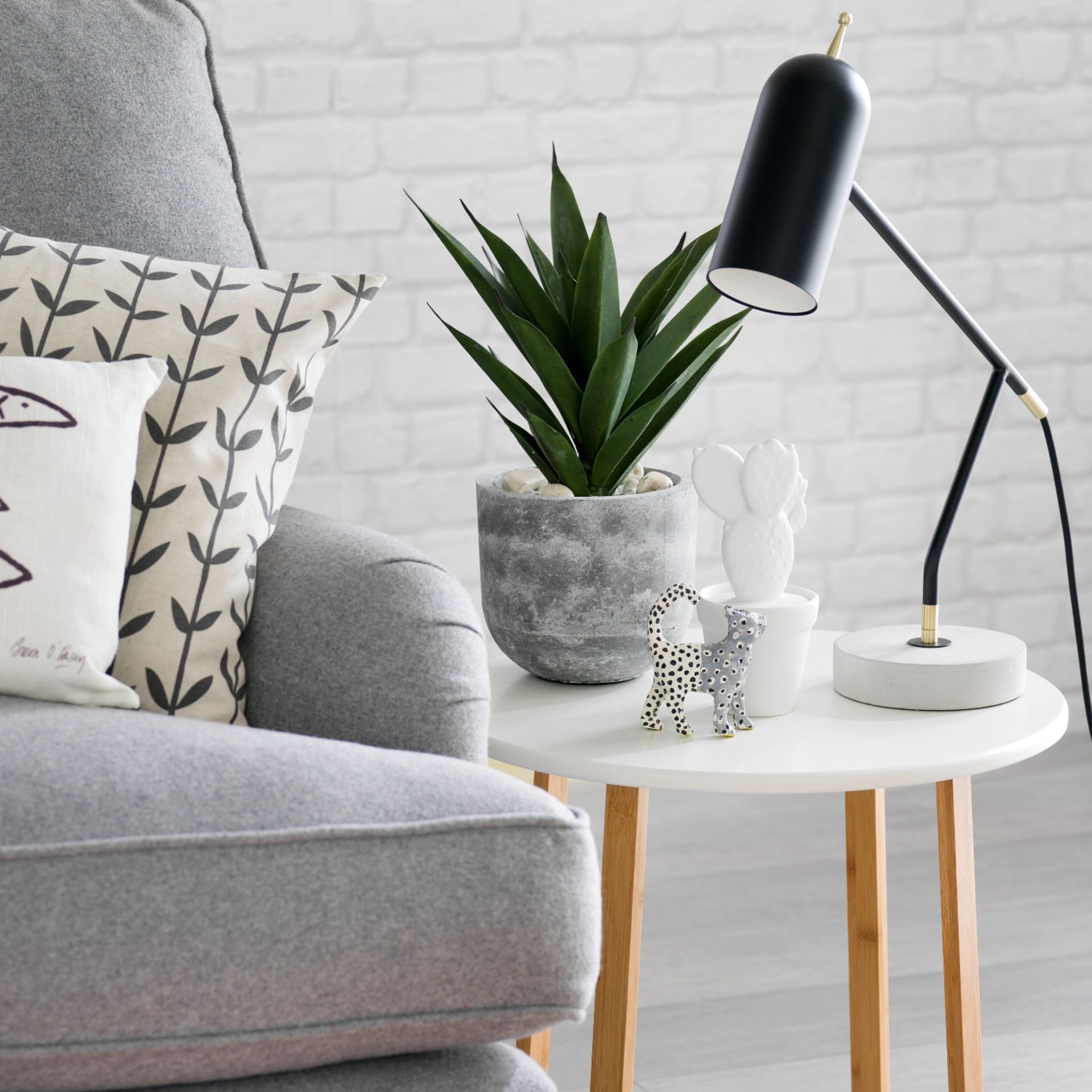 grey sofa with patterned cushions next to white small table with plant, table lamp and decor