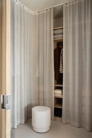 walk-in closet with sheer curtain doors, a white ottoman, and the edge of a timber door visible