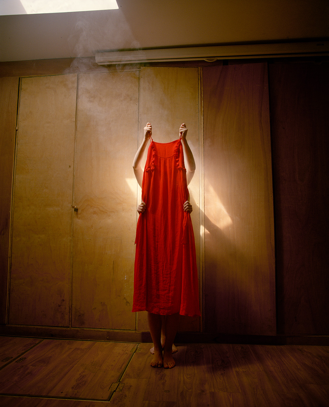 Colour photograph of a two unidentified people holding up a red dress
