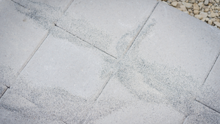 polymeric sand on grey outdoor tiles with pebbles in top right corner