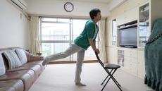 woman in indoors standing on one leg while holding the back of a chair.