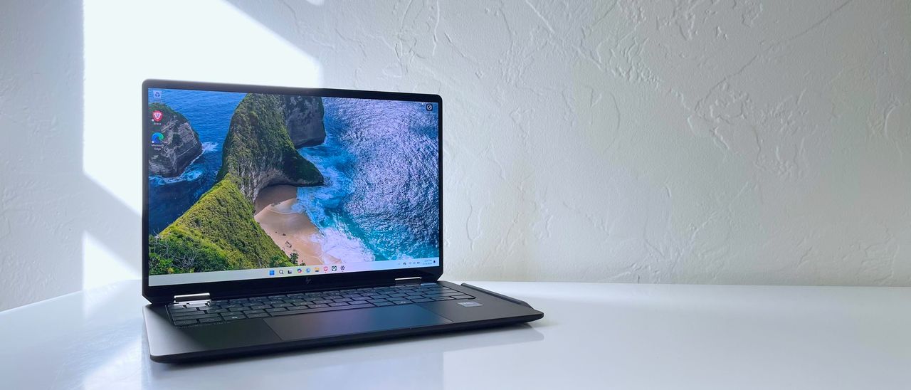 An open and powered on laptop on top of a white table, showing a image of green hills leading to an ocean shore.
