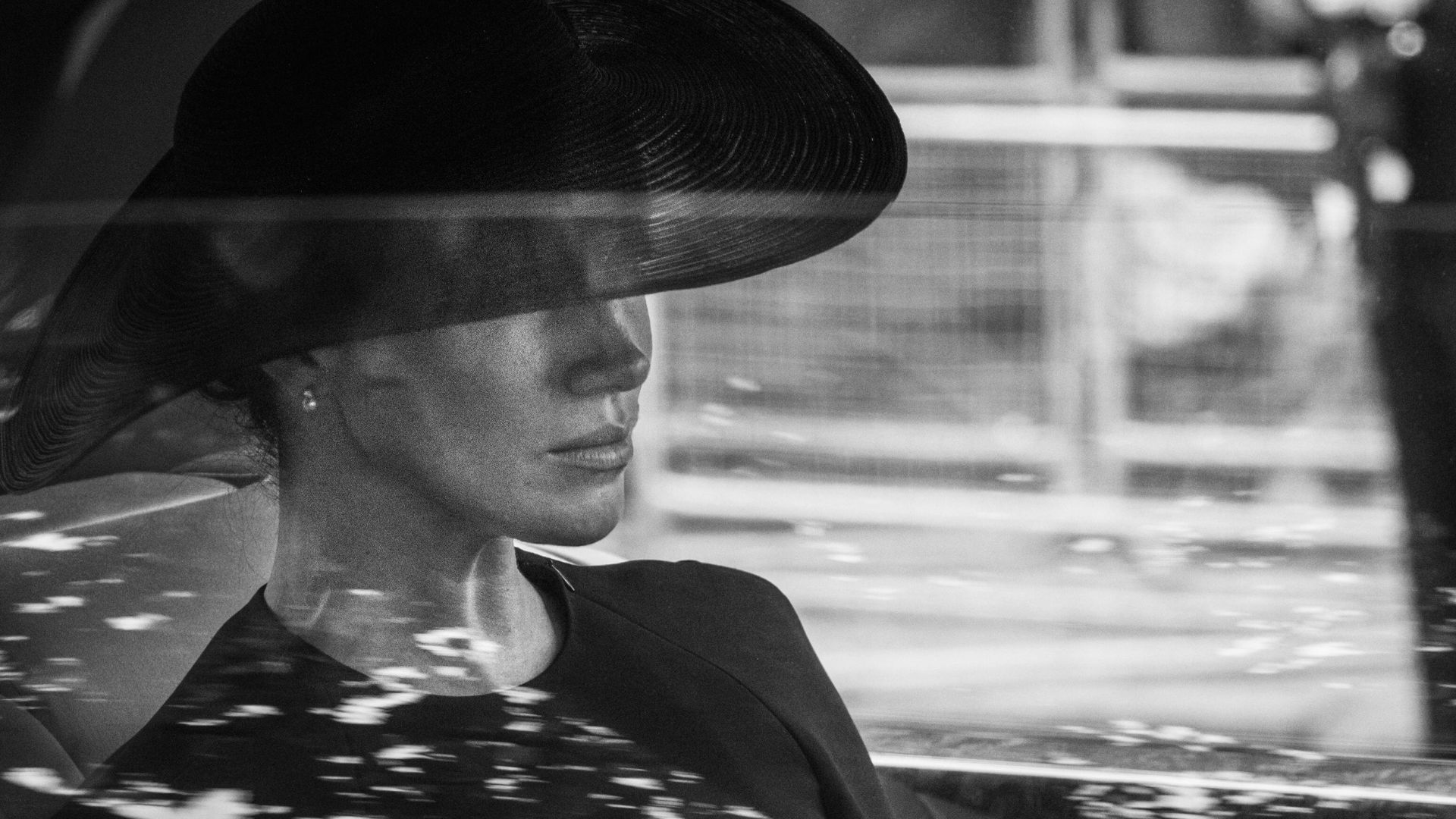 A black and white image of a solemn looking Meghan Sussex inside a car