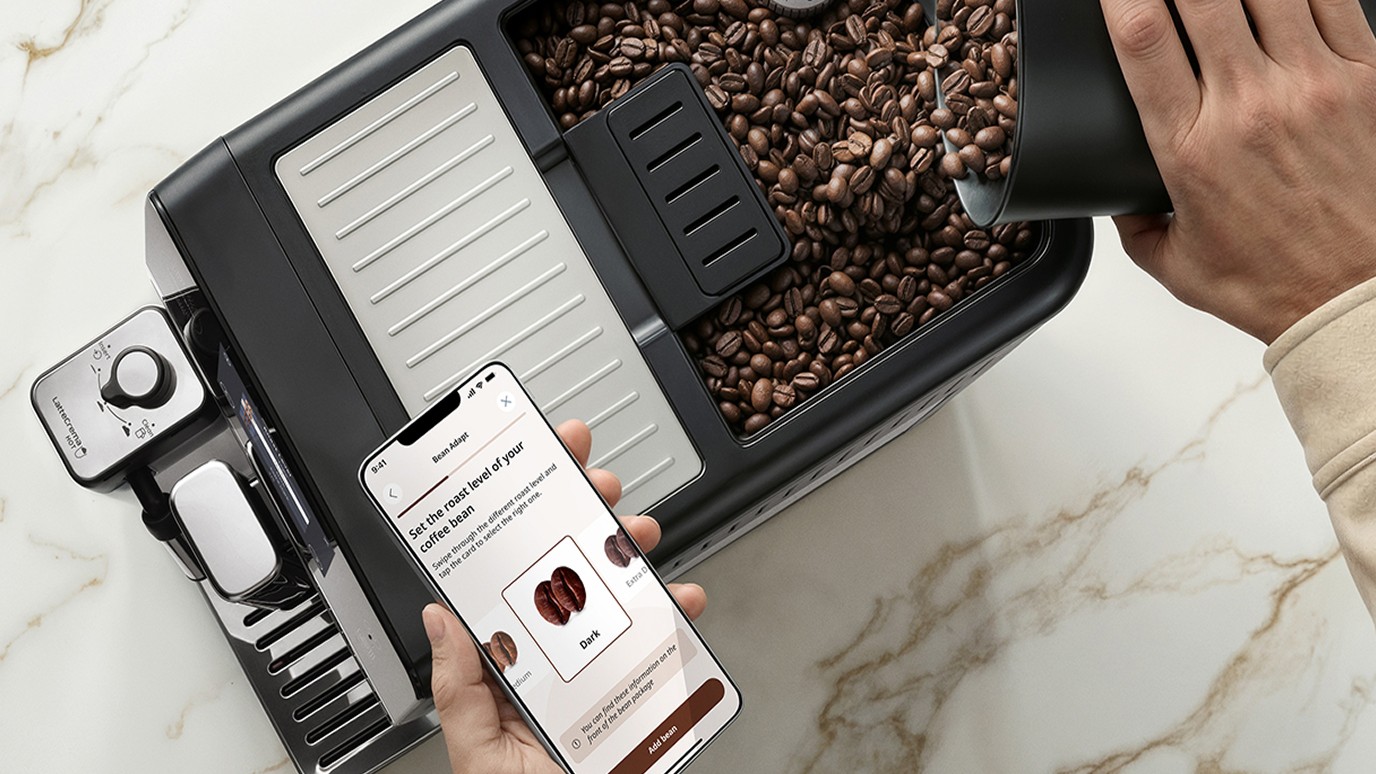 Person pouring coffee beans into De'Longhi Eletta Ultra coffee maker while using mobile app