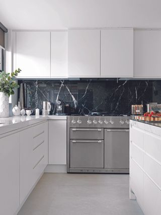 A small bright white gloss kitchen with steel oven and black marble backsplash
