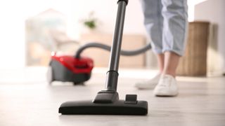 A red canister vacuum cleaner being used on a hard floor