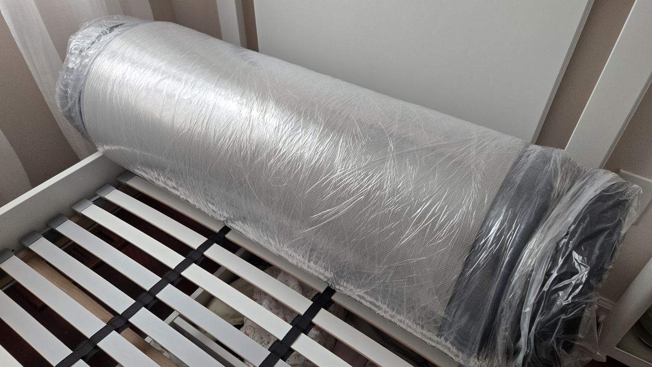 DreamCloud Classic Memory Foam Mattress rolled up in plastic at the head of a platform bed