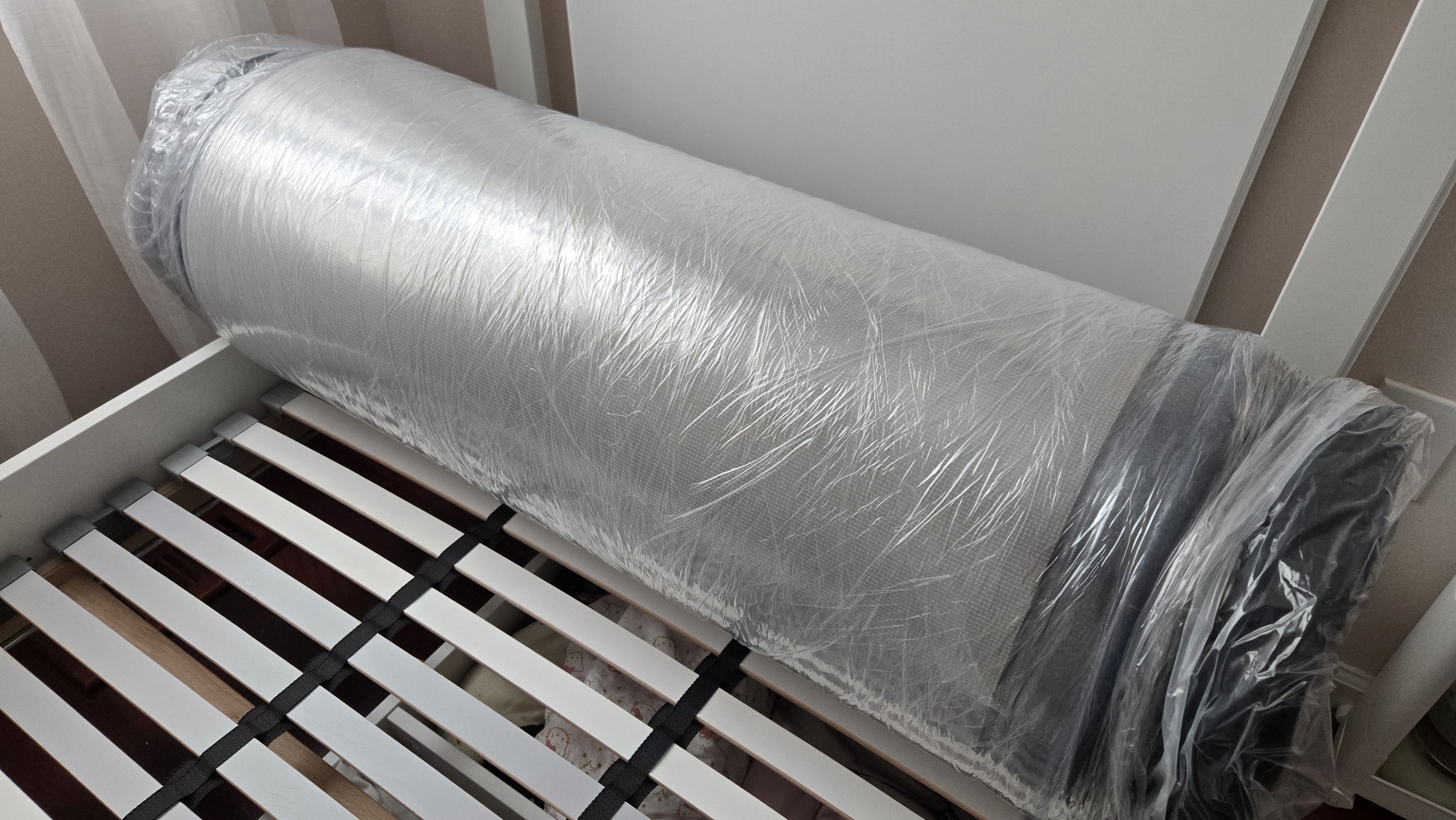 DreamCloud Classic Memory Foam Mattress rolled up in plastic at the head of a platform bed