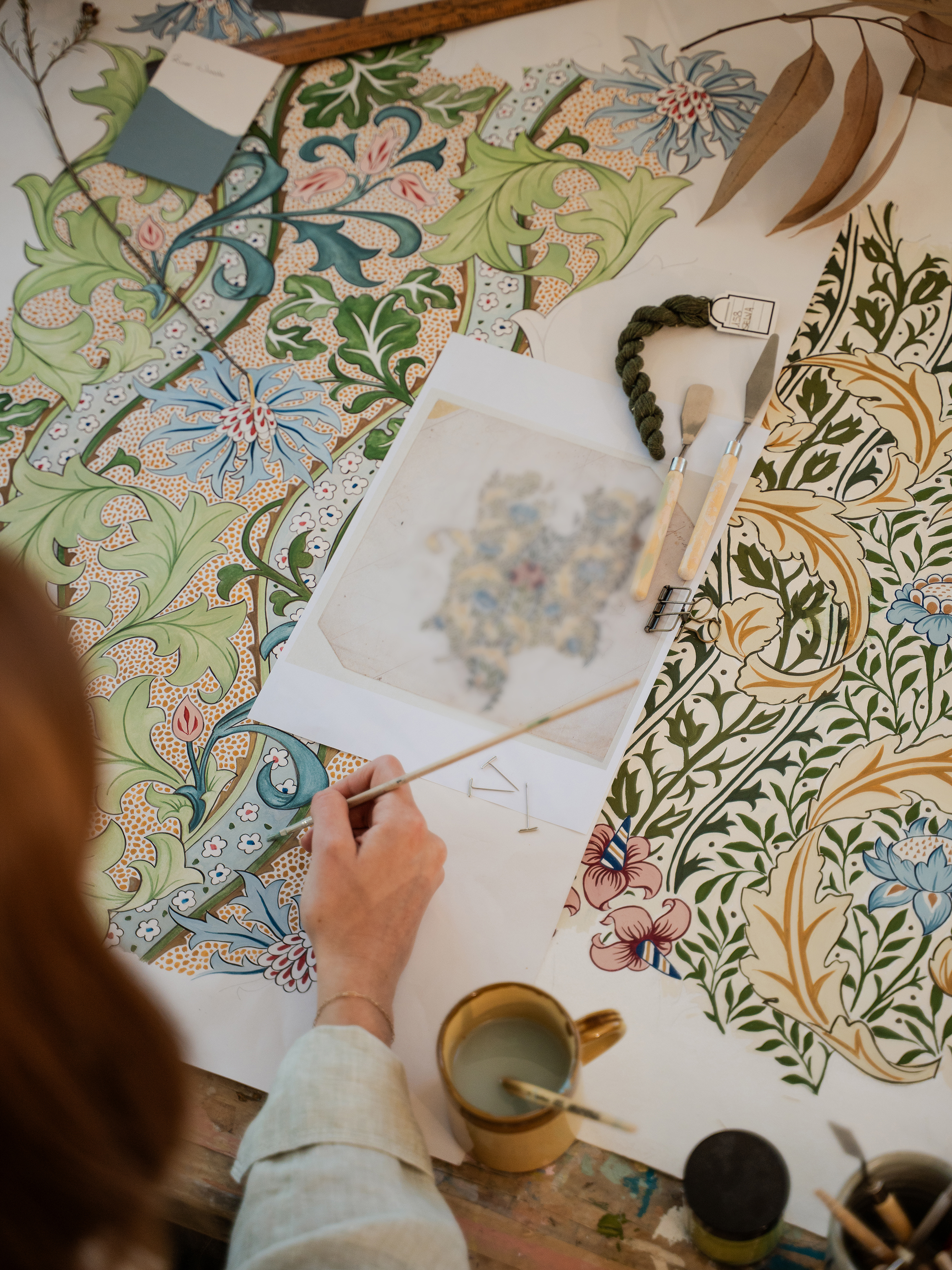 A woman's hand covers over an original Morris print and a replica holding a paintbrush