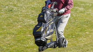 The black and yellow PowaKaddy Dri Tech Cart Bag on a trolley on the golf course