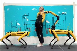 a woman stands next to two dog-like robots