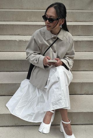A woman's white dress outfit with a high neck poplin dress layered under a cropped trench coat and white Tabi pumps.