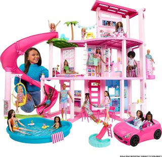 A smiling child kneels on the floor to play with the Barbie Dreamhouse