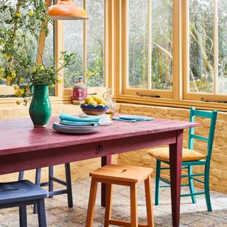 Burgundy painted table surrounded by colourful chairs and stools