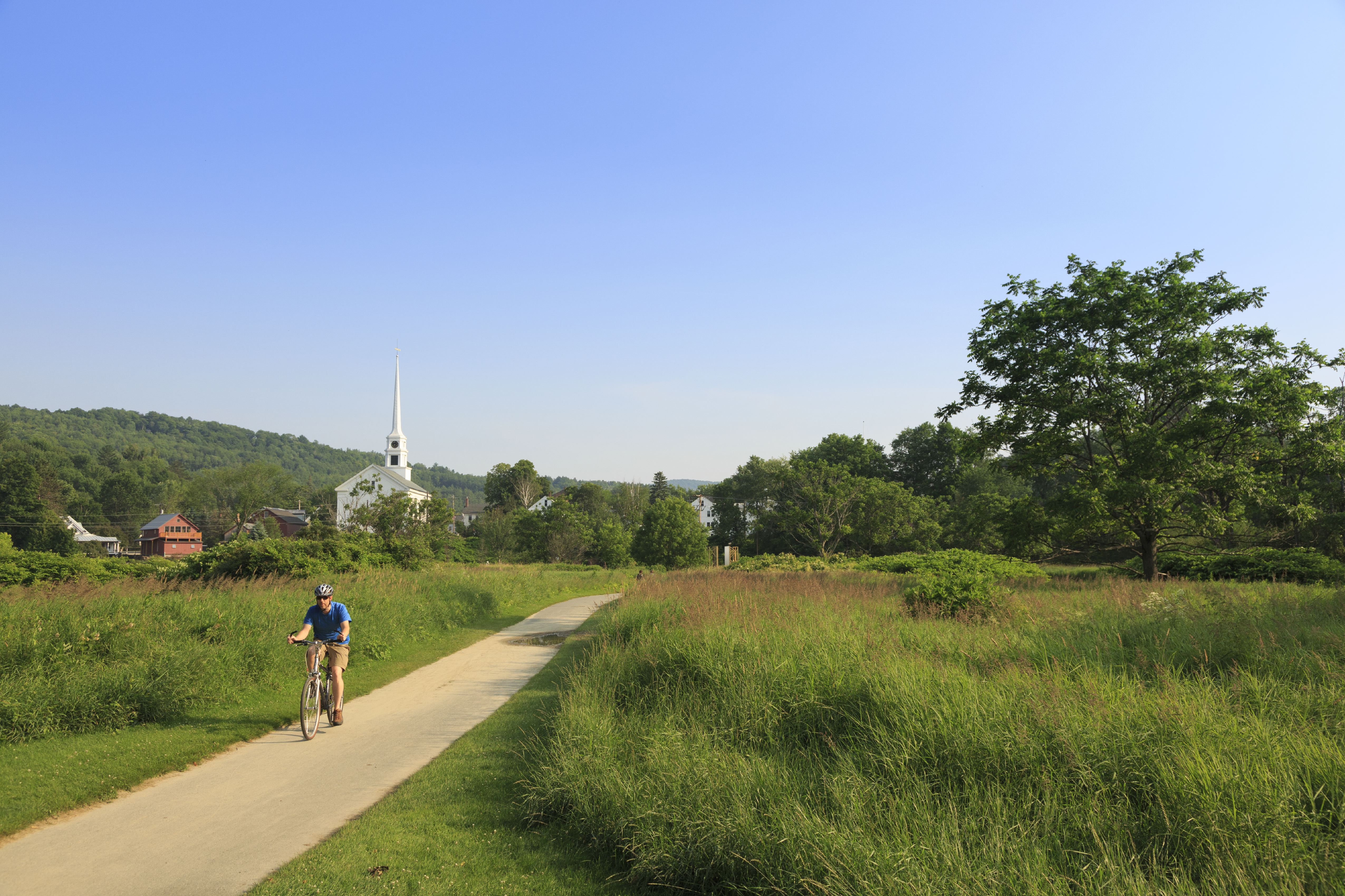 A man rides his bike down the paved Stowe Recreation Path on a sunny day in Stowe, Vermont