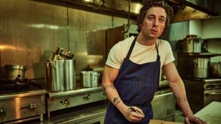 Carmy (Jeremy Allen White) leans on a kitchen counter in his classic white t-shirt and apron in The Bear season 3