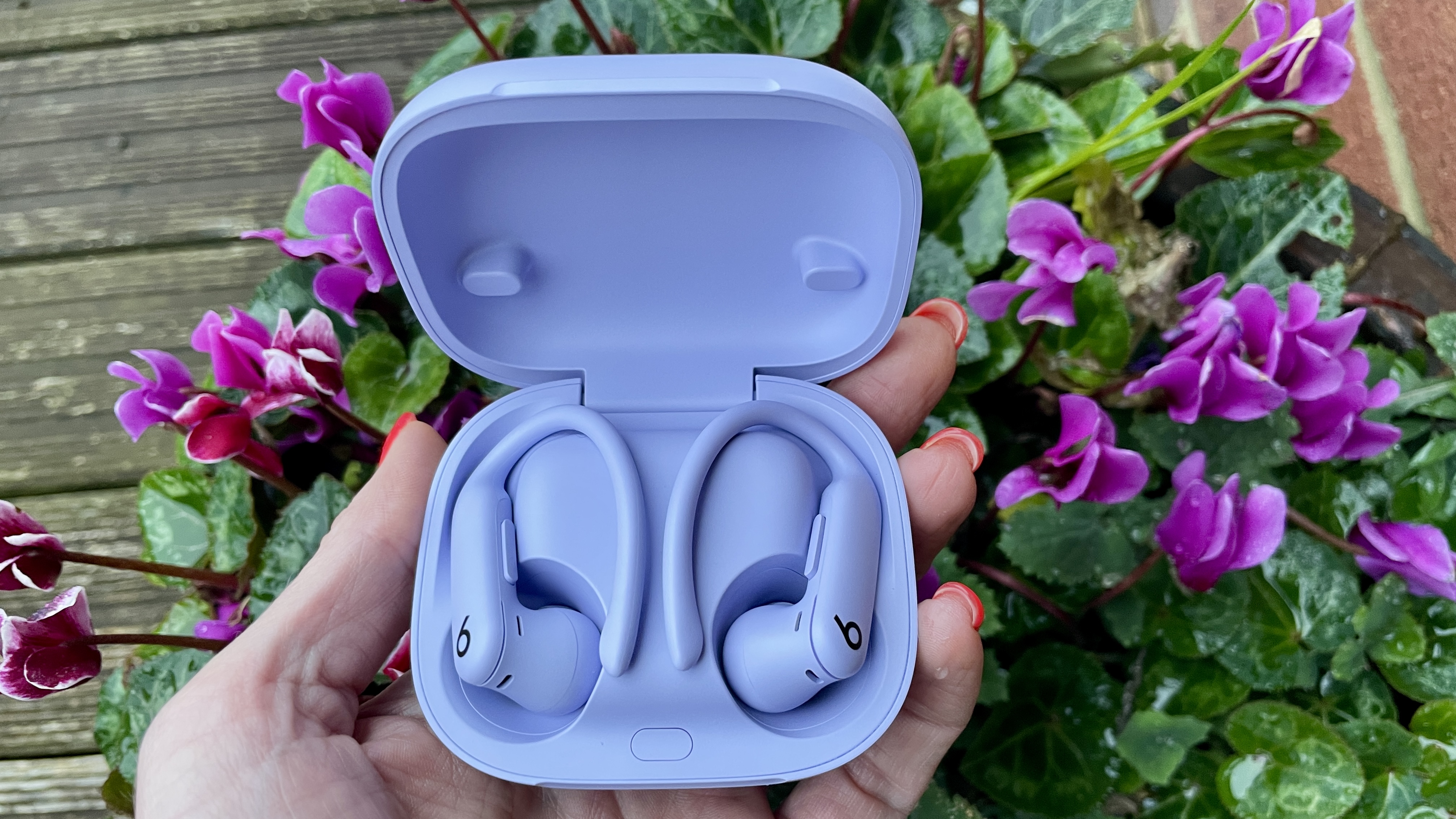 Beats Powerbeats Pro 2 outside on a rainy day, held in a hand and close to a flower-bed