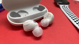 Sony WF-C700N wireless earbuds out of their case on a red background