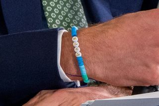 A closeup of Prince William's wrist showing a blue and green beaded friendship bracelet reading PAPA.