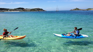 Two people in single kayaks paddle out to sea from St Mary's