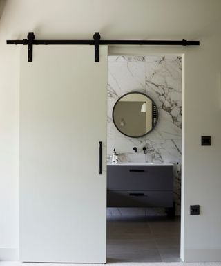 A white barn door opening up to a black-and-white powder room