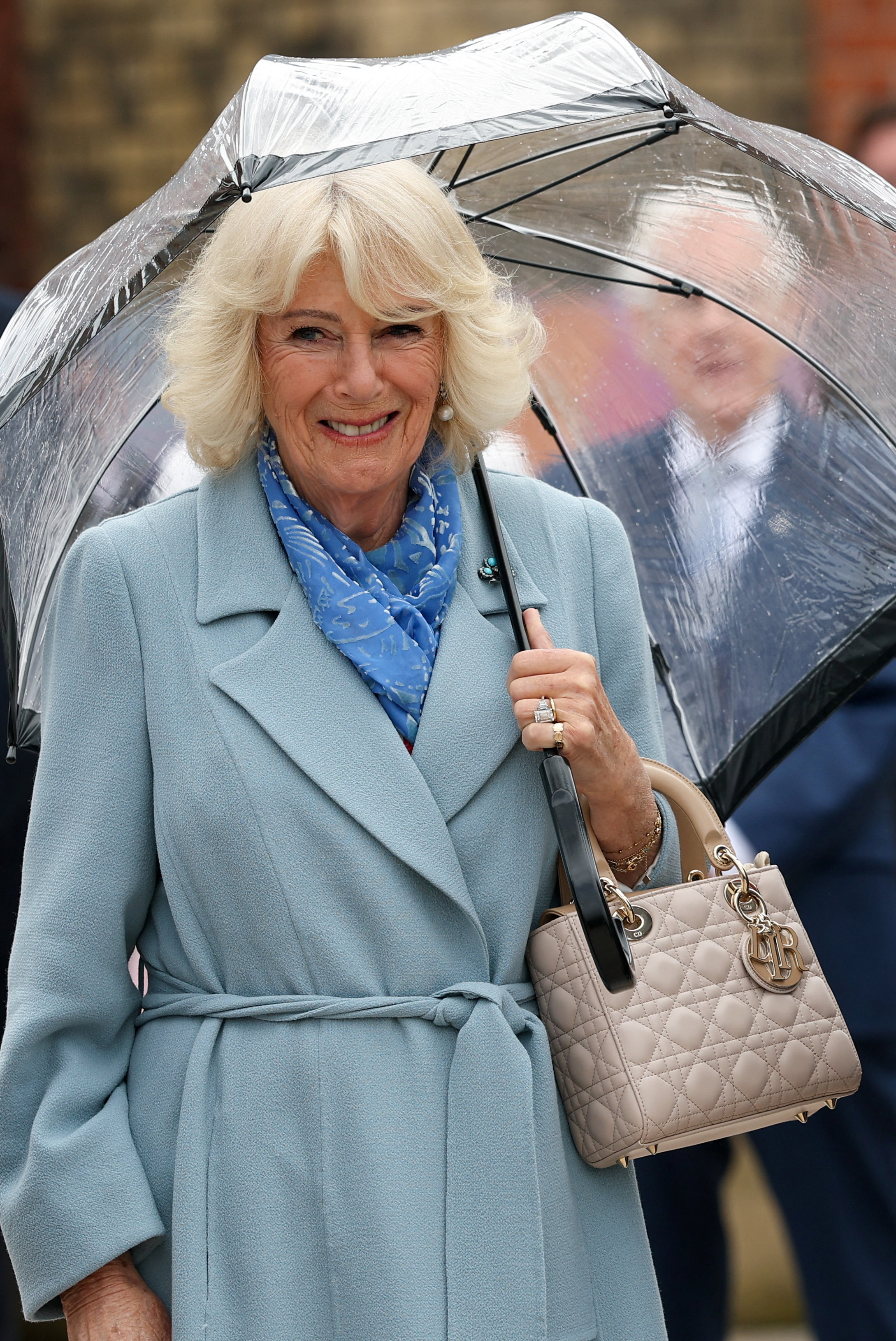 Queen Camilla wearing a blue coat holding an umbrella