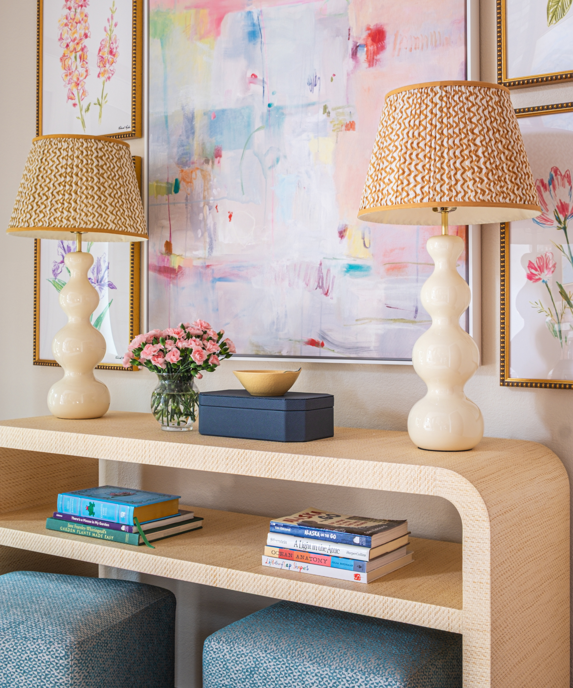 a console table with two matching lamps, a box, a vase of flowers, and two stacks of books