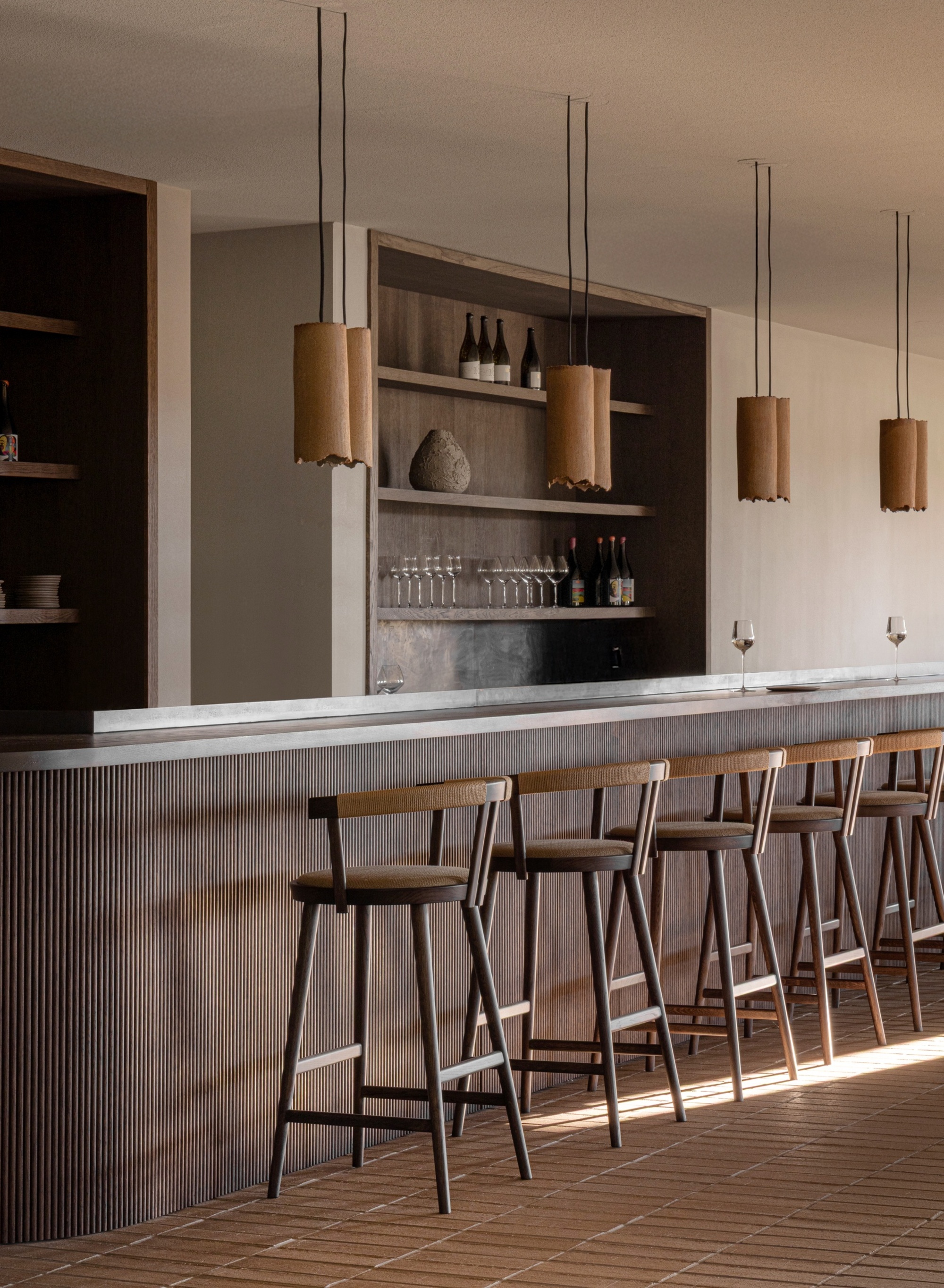 A scandi kitchen with a ribbed island, bar stools, wooden details, and pendant lights above the island