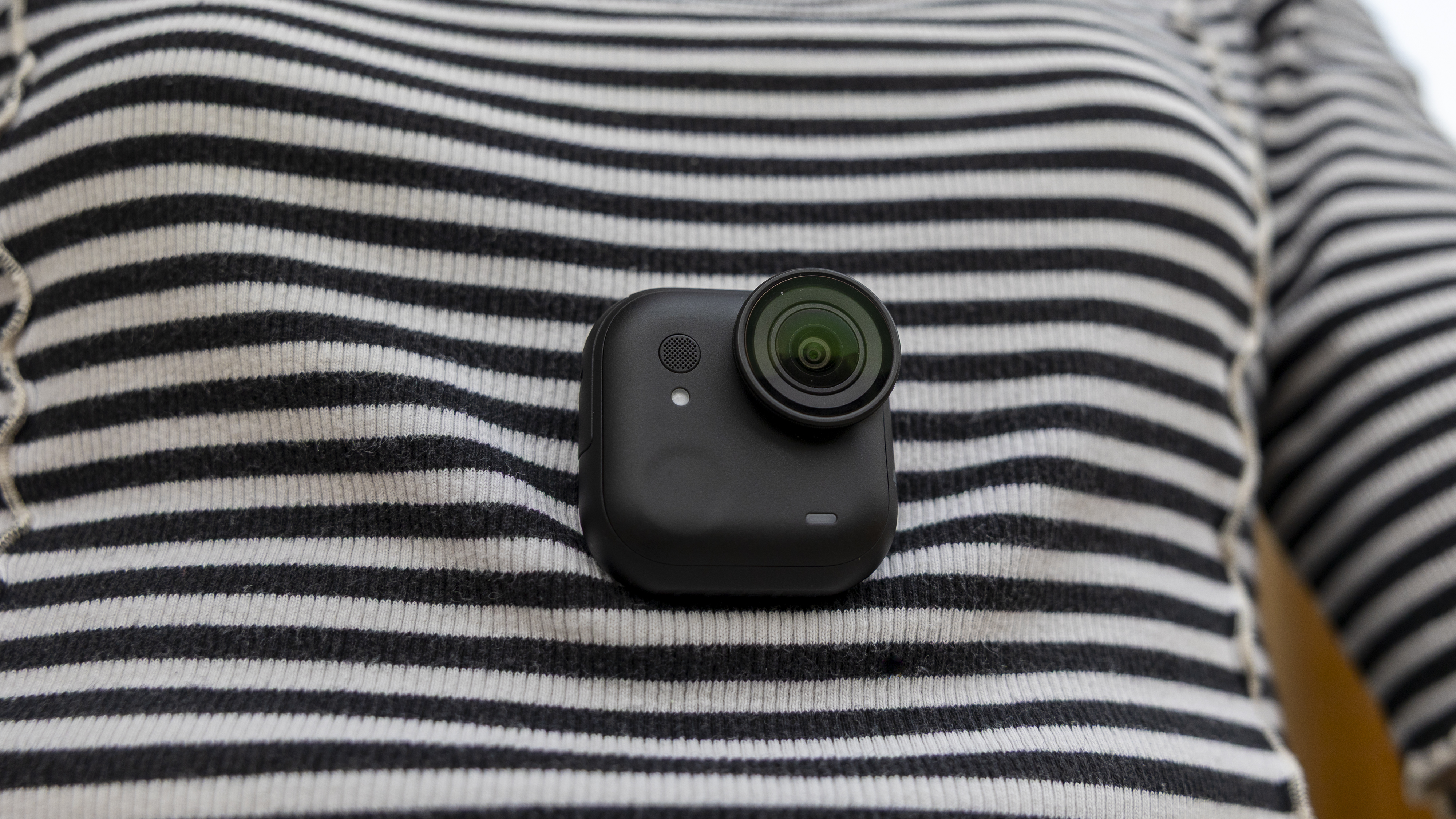 A female photographer in a stripy top wearing the Insta360 GO Ultra using the magnet pendant underneath