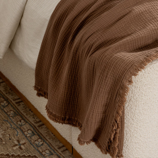 A rusty brown throw blanket over the side of a bed.