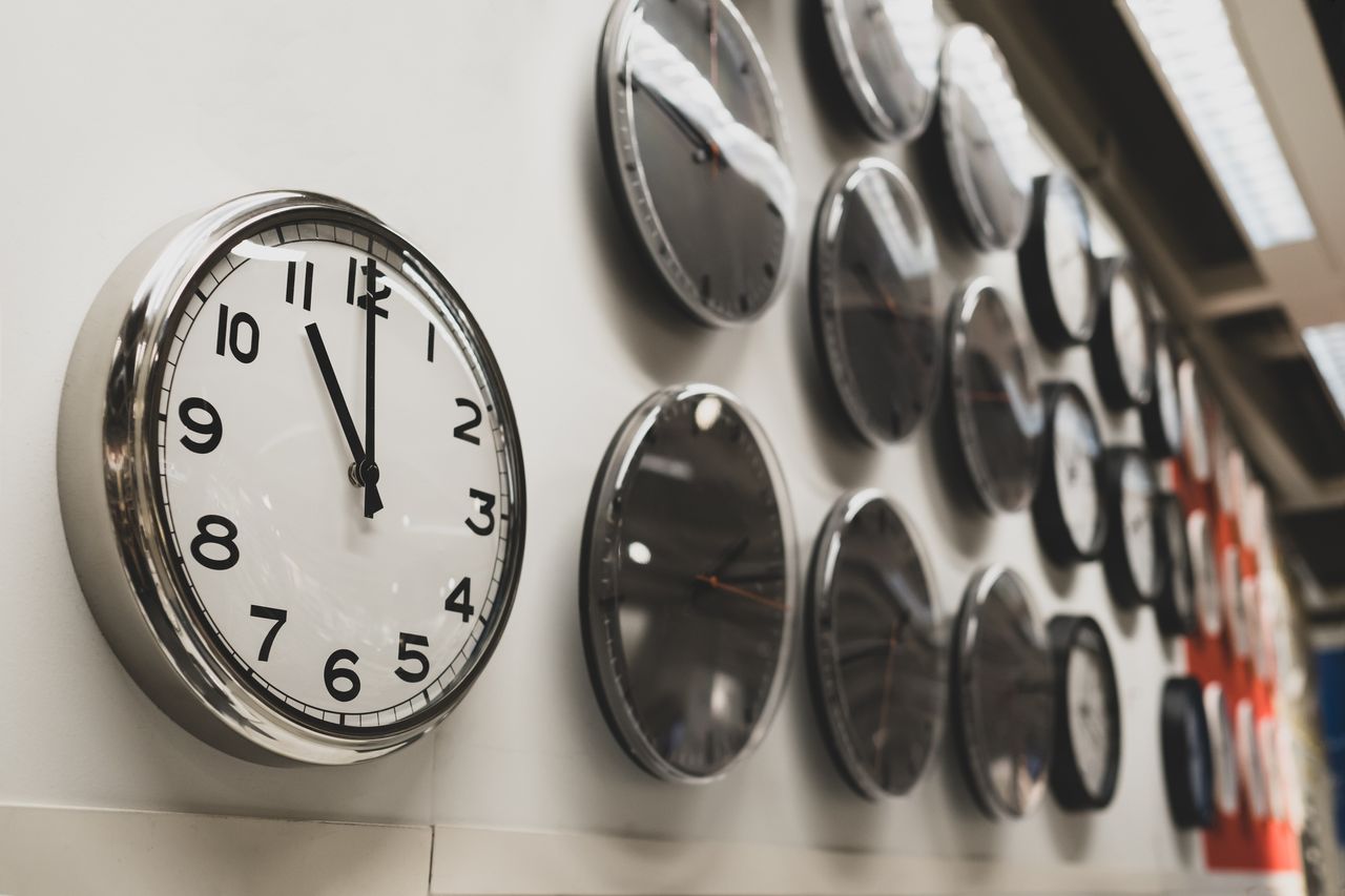 a wall of analog clocks with the closest one reading 11 o&#039;clock