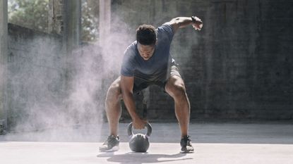 A man training outdoors performing a kettlebell clean