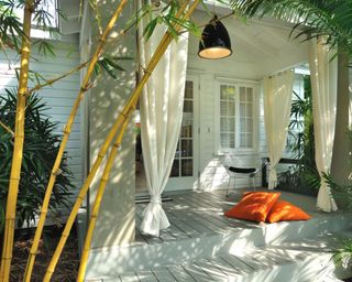 A white painted front porch with decking, shade, and curtains