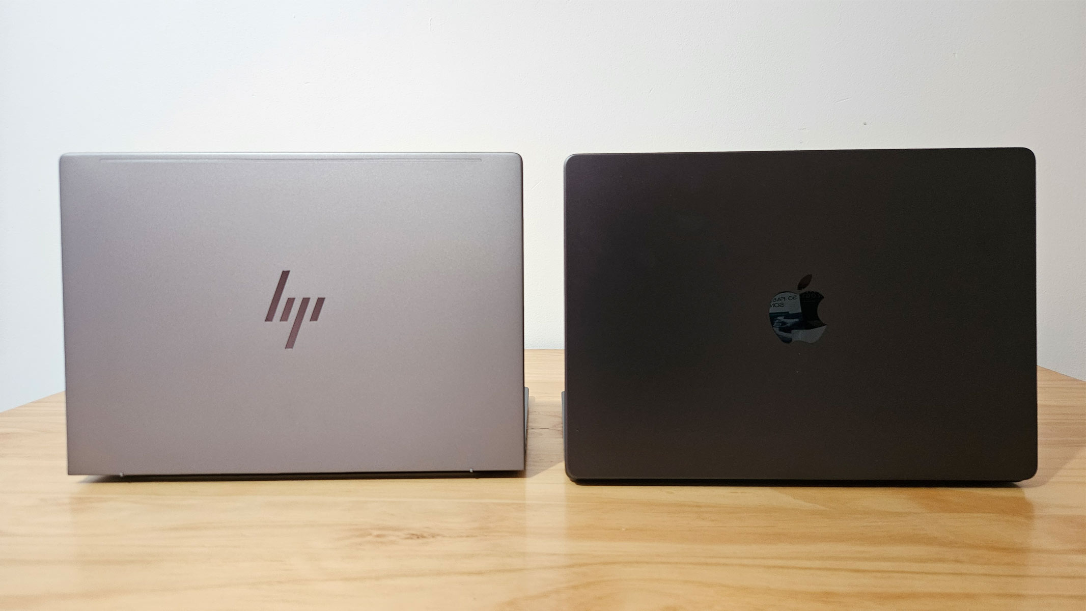 A MacBook and HP laptop placed side-by-side on a wooden table, showing their respective logos.