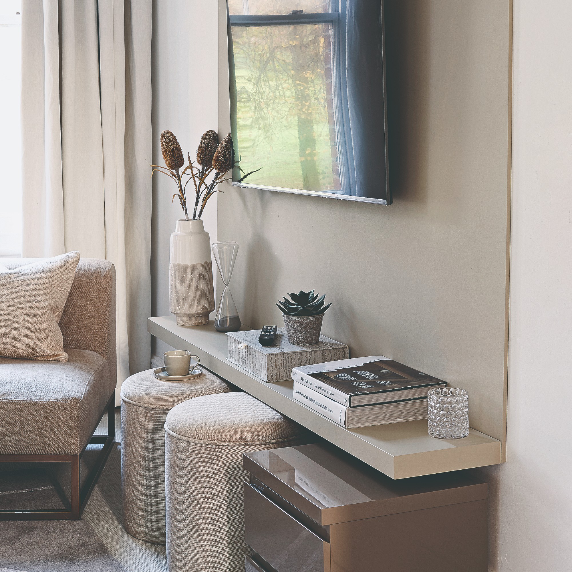 A tidy neutral-coloured living room with a TV on the wall