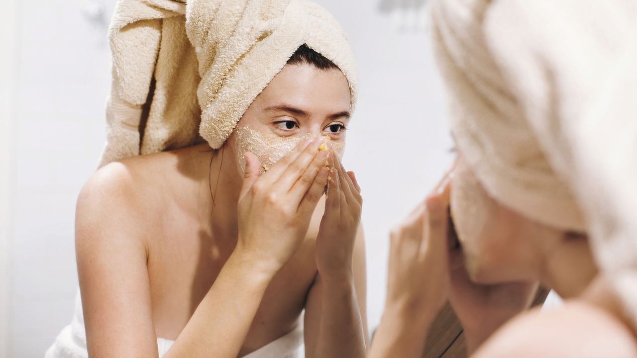 woman with a towel on her head applying a diy face mask at home