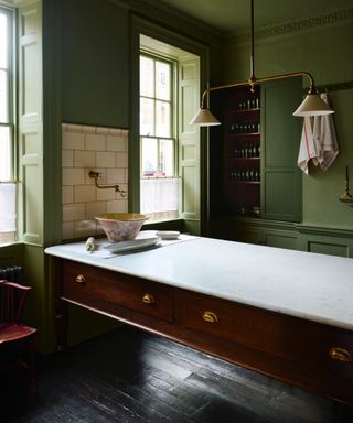 Green kitchen with vintage table as island, marble countertop, dark wood flooring,